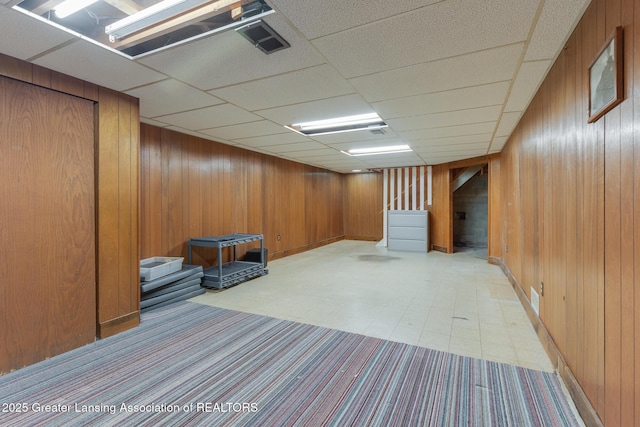 finished below grade area with stairway, wood walls, baseboards, and visible vents