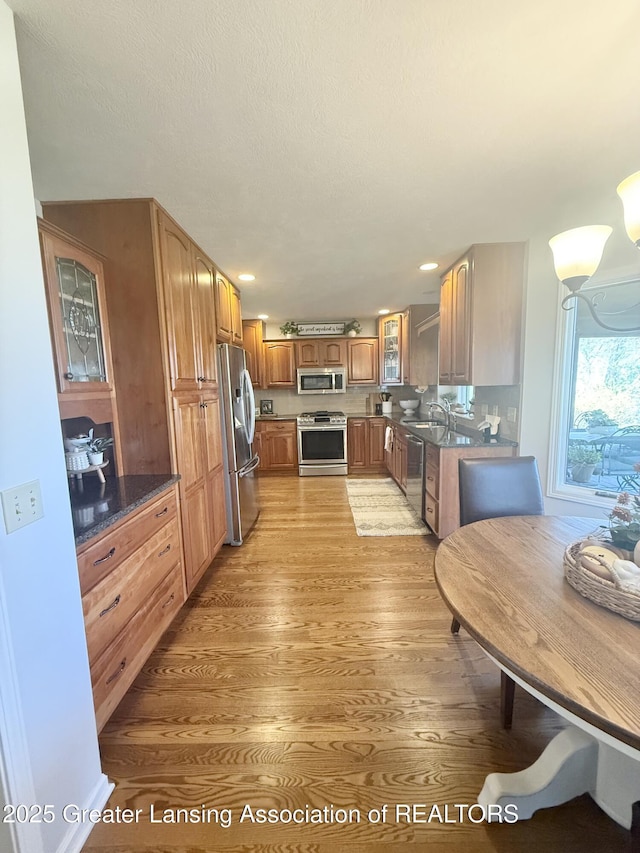 kitchen featuring appliances with stainless steel finishes, brown cabinets, a sink, glass insert cabinets, and light wood-style flooring