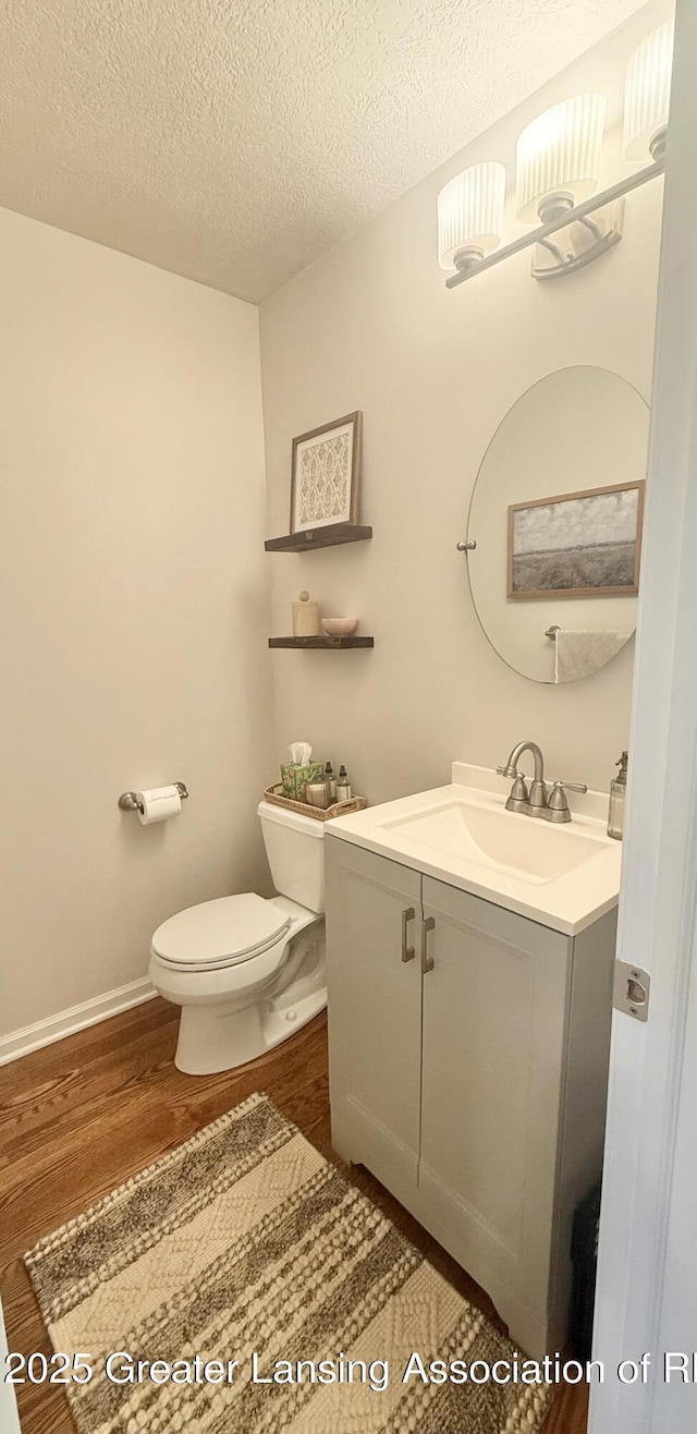 half bath featuring a textured ceiling, wood finished floors, vanity, baseboards, and toilet