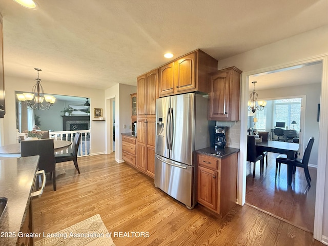 kitchen with an inviting chandelier, stainless steel fridge with ice dispenser, brown cabinetry, and light wood finished floors