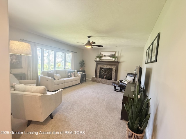 carpeted living room with a fireplace with raised hearth and a ceiling fan