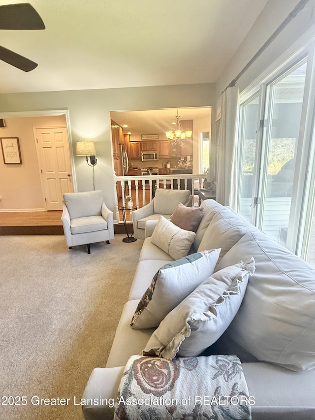 living room with baseboards, carpet, and ceiling fan with notable chandelier