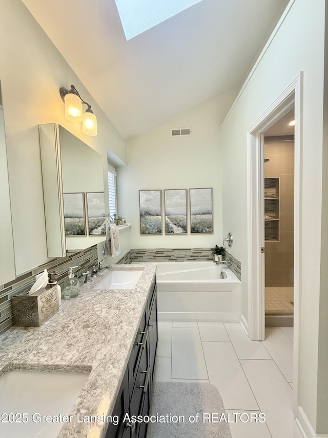 bathroom with tile patterned flooring, a garden tub, visible vents, lofted ceiling with skylight, and a sink