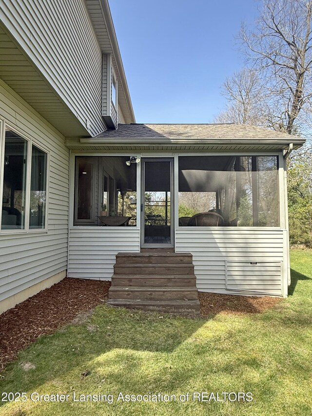 doorway to property featuring roof with shingles and a lawn