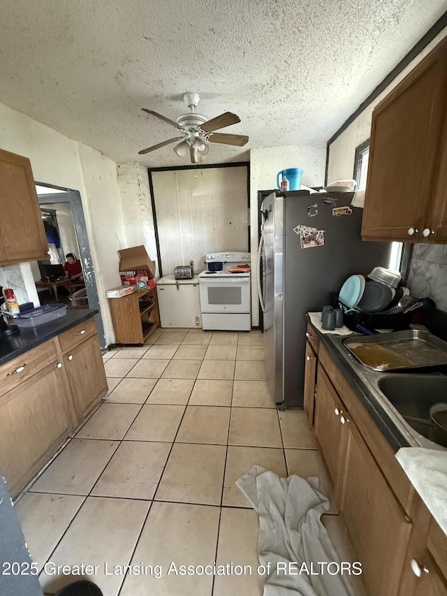 kitchen featuring brown cabinetry, a ceiling fan, a sink, light tile patterned flooring, and electric stove