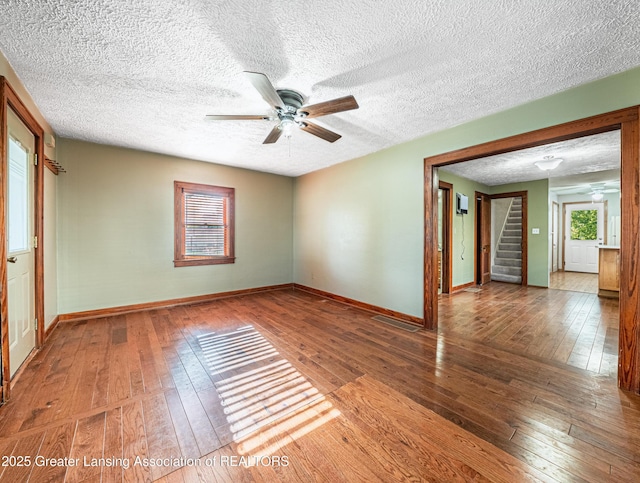 spare room featuring wood-type flooring, baseboards, ceiling fan, and stairway