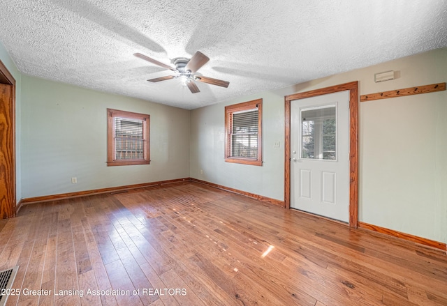 unfurnished room with ceiling fan, wood-type flooring, a textured ceiling, baseboards, and visible vents