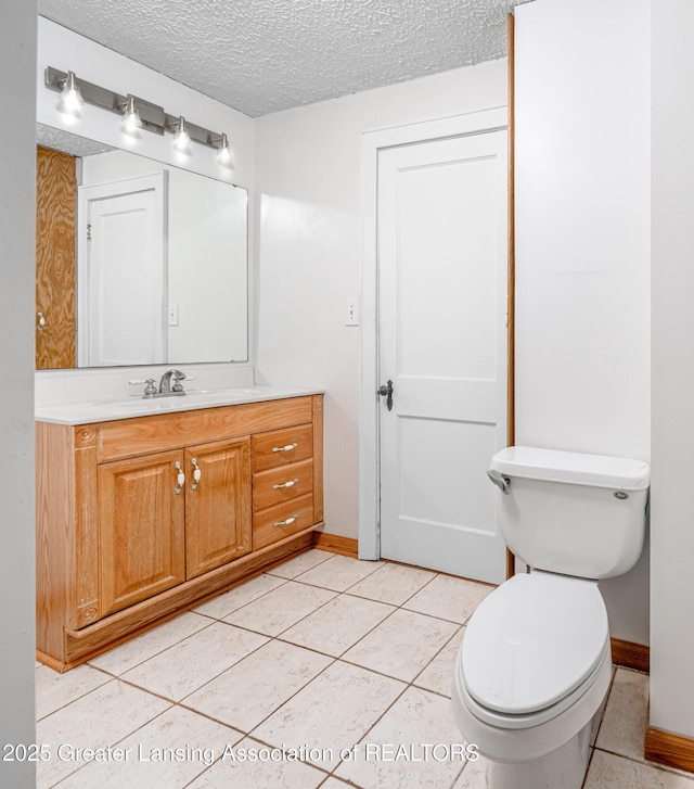 bathroom with tile patterned flooring, vanity, toilet, a textured ceiling, and baseboards