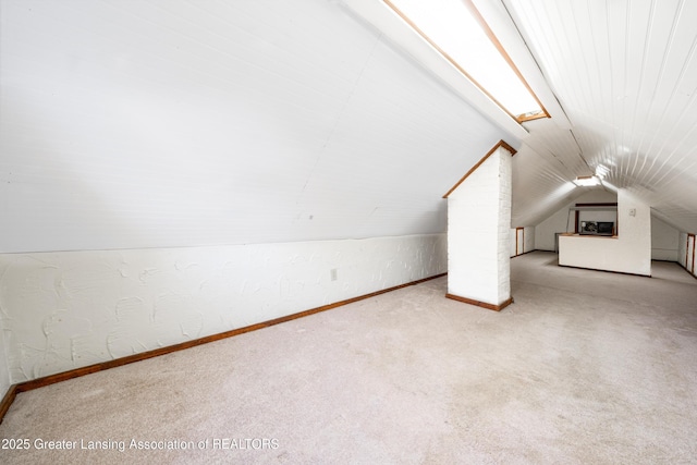 additional living space featuring carpet floors, baseboards, vaulted ceiling, and a textured wall