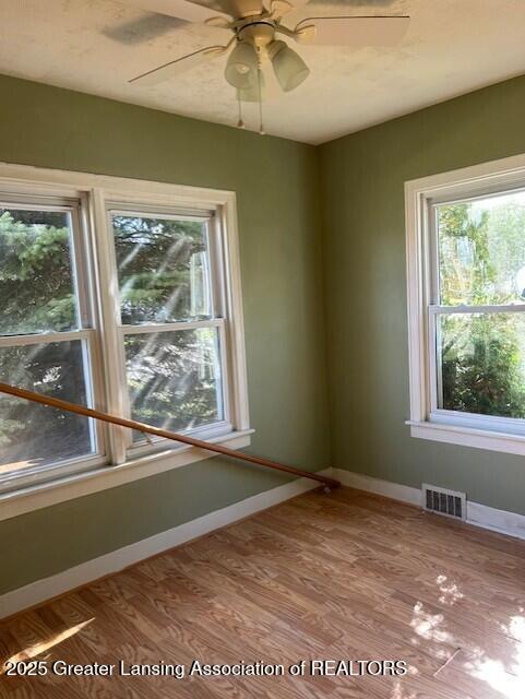 unfurnished room with baseboards, a ceiling fan, wood finished floors, and visible vents