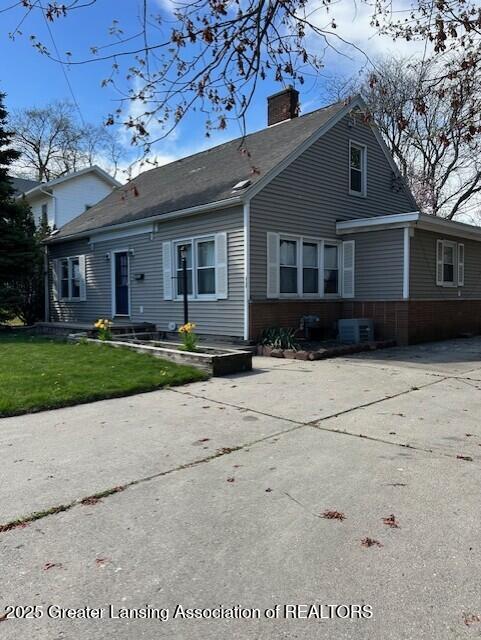 view of front of home featuring a shingled roof, a chimney, cooling unit, and a front lawn