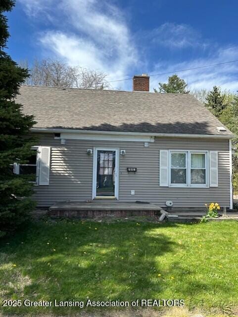 back of property with a lawn, a chimney, and roof with shingles