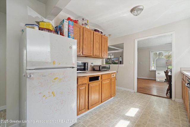 kitchen with freestanding refrigerator, stainless steel microwave, a toaster, and light countertops