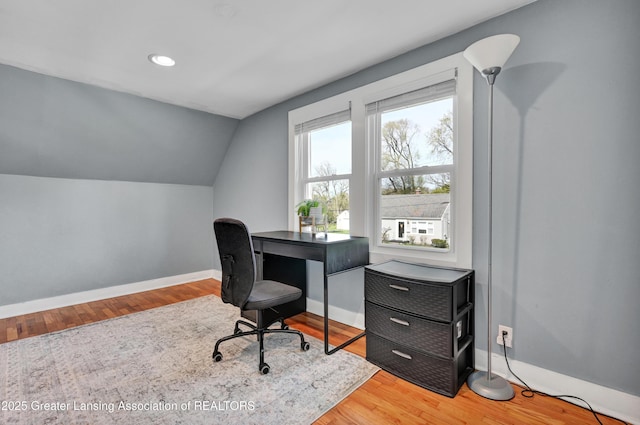 office area with baseboards, vaulted ceiling, and light wood-type flooring