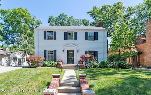 colonial-style house featuring a chimney and a front lawn