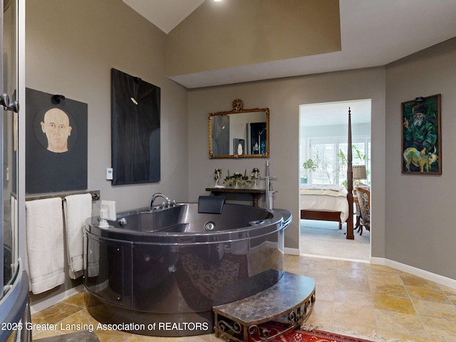ensuite bathroom featuring a tub with jets, connected bathroom, lofted ceiling, and baseboards