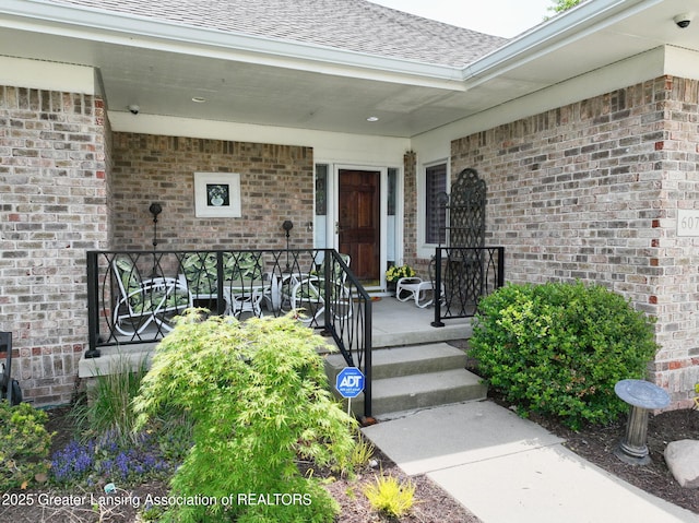 6074 E Longview Dr, East Lansing, MI 48823 - view of exterior entry with brick siding, roof with shingles, covered porch, and a surveillance system