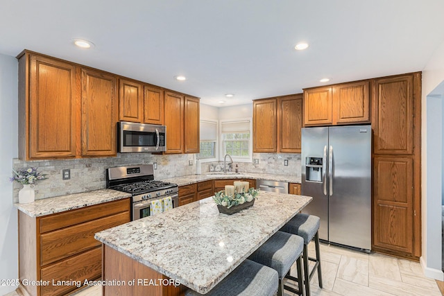 kitchen featuring a kitchen bar, light stone countertops, brown cabinets, a sink, and stainless steel appliances