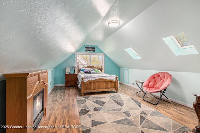 bedroom featuring vaulted ceiling with skylight, a textured ceiling, visible vents, wood finished floors, and baseboards