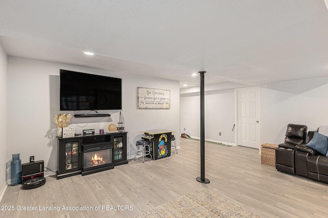 living room featuring recessed lighting, baseboards, a glass covered fireplace, and wood finished floors