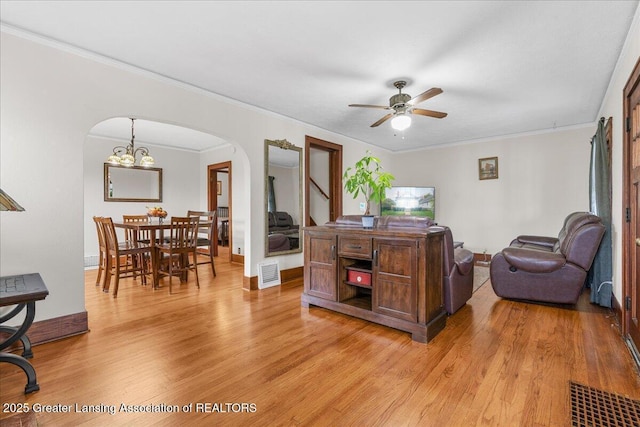 living room with light wood-style floors, arched walkways, a ceiling fan, and crown molding