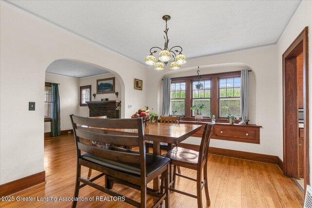 dining space with baseboards, a notable chandelier, light wood finished floors, and arched walkways