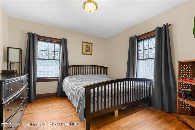 bedroom featuring baseboards, light wood finished floors, and multiple windows