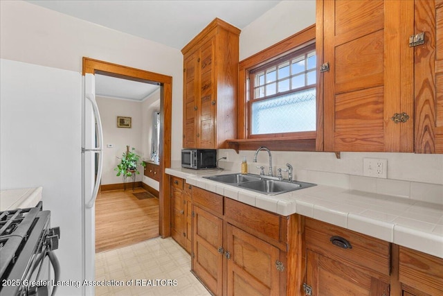 kitchen featuring baseboards, light floors, brown cabinets, a sink, and stainless steel appliances