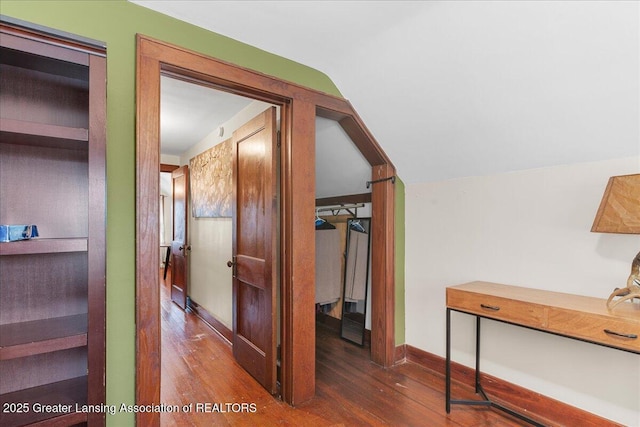 hallway featuring baseboards, lofted ceiling, and wood finished floors