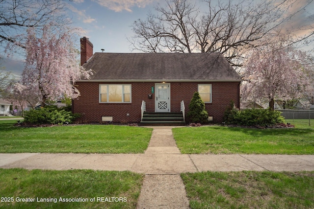 view of front of home featuring fence, a shingled roof, a front lawn, brick siding, and a chimney