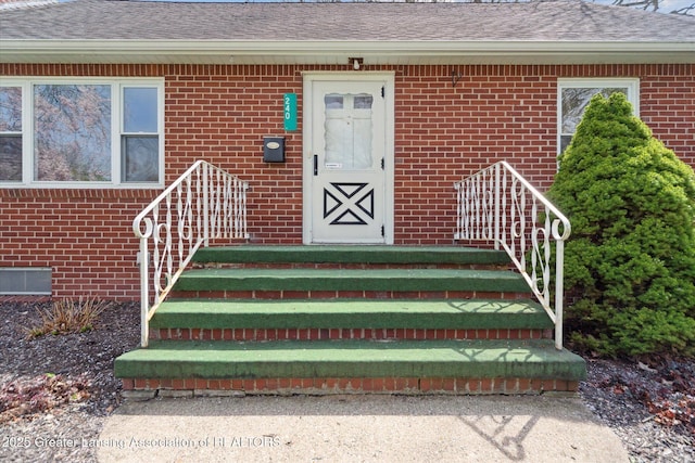 entrance to property with roof with shingles and brick siding