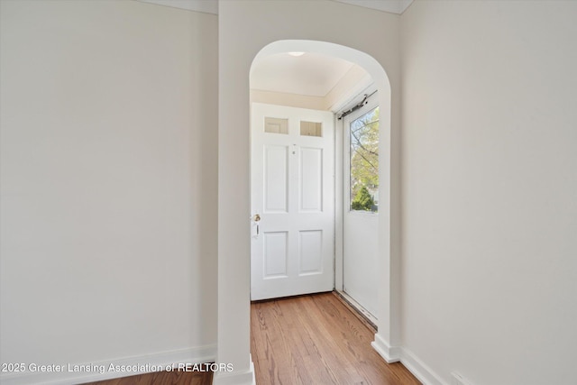 entryway featuring baseboards, arched walkways, and light wood finished floors