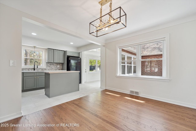 kitchen with an inviting chandelier, visible vents, a healthy amount of sunlight, light wood-type flooring, and gray cabinets