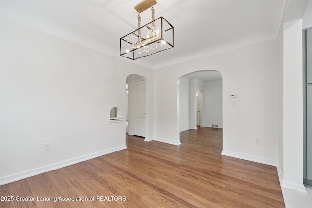 unfurnished dining area featuring arched walkways, baseboards, a chandelier, and light wood-type flooring
