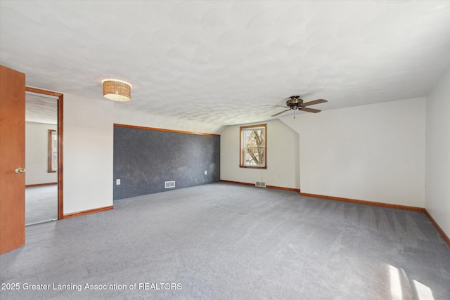 interior space featuring carpet flooring, a ceiling fan, baseboards, lofted ceiling, and visible vents