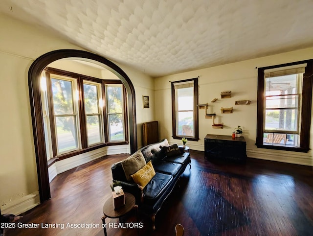 living area with baseboards, arched walkways, and wood finished floors