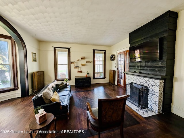 living area with baseboards, a fireplace, arched walkways, and wood finished floors
