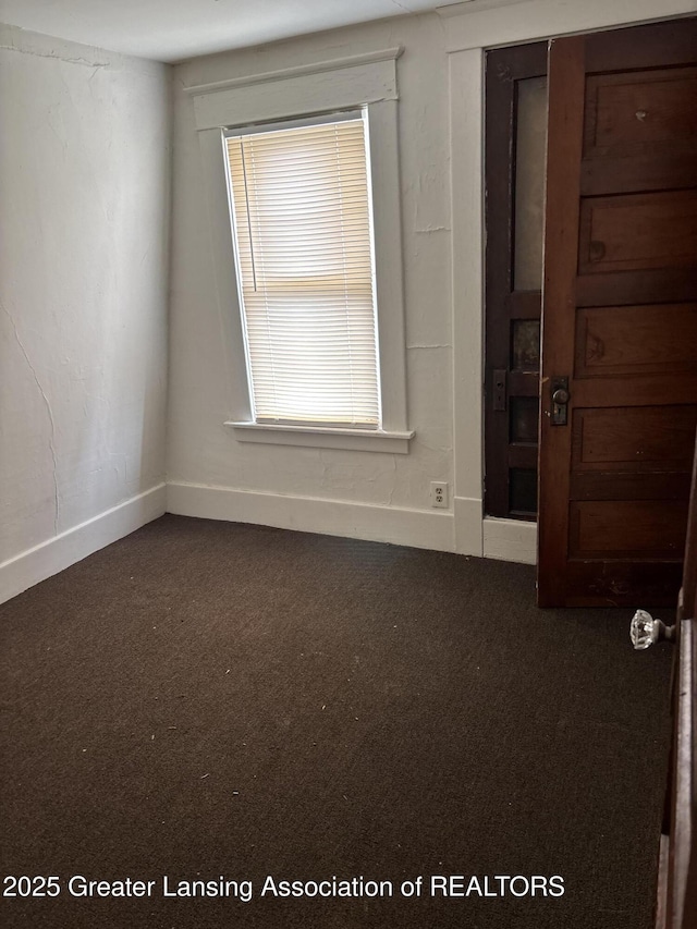 unfurnished room with dark colored carpet and baseboards