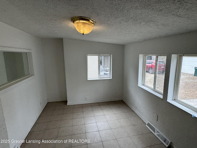 spare room featuring a textured ceiling, visible vents, a healthy amount of sunlight, and tile patterned flooring