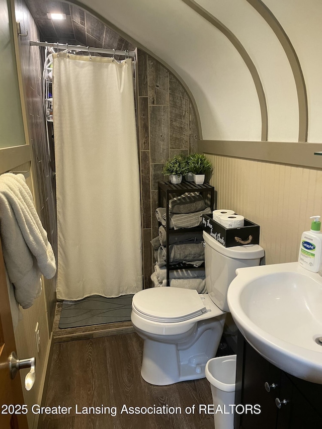 full bathroom featuring curtained shower, wood finished floors, toilet, a wainscoted wall, and a sink