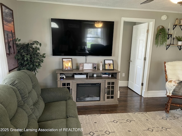 living area featuring baseboards, ornamental molding, a ceiling fan, and wood finished floors