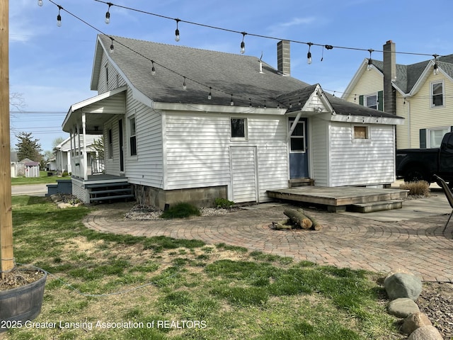 rear view of house featuring a shingled roof, a yard, covered porch, and a chimney