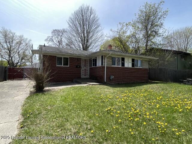 ranch-style home with brick siding, a front lawn, fence, and driveway