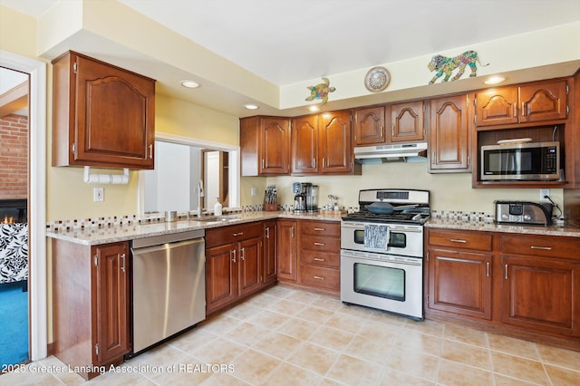 kitchen featuring light stone countertops, recessed lighting, under cabinet range hood, a sink, and appliances with stainless steel finishes