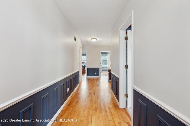 corridor with visible vents, light wood-style flooring, attic access, and a wainscoted wall