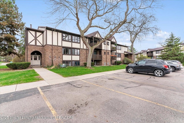 view of front of house featuring a front lawn, uncovered parking, stucco siding, brick siding, and a residential view