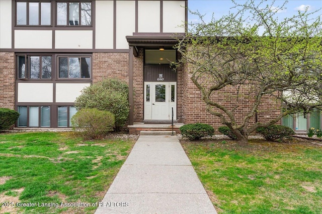 view of exterior entry with a yard, brick siding, and stucco siding
