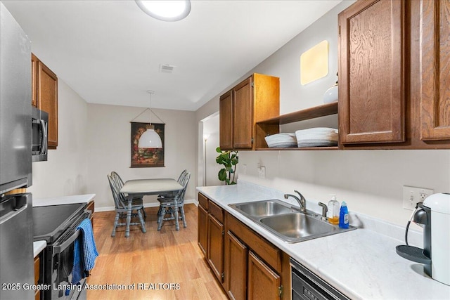 kitchen featuring appliances with stainless steel finishes, open shelves, a sink, light countertops, and light wood finished floors