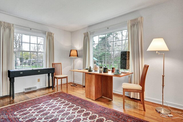 office space featuring baseboards, visible vents, plenty of natural light, and wood finished floors