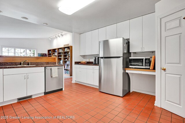 kitchen featuring dark countertops, appliances with stainless steel finishes, a sink, vaulted ceiling, and visible vents